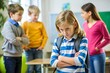 © sandipruel - A girl with a blue and white striped shirt is standing in front of a group of children. She looks upset and is crossing her arms.