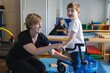 © Peakstock - Bobath therapist assists a young boy with cerebral palsy as he practices using a supportive mobility device during a session