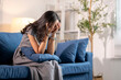 © Wasana - Young woman feeling sad while sitting on sofa at home