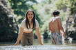 © qunica.com - Happy young friends enjoying a sunny day wading in a refreshing natural stream surrounded by lush greenery.