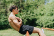 © qunica.com - Fit strong male athlete working out in park, demonstrating core exercises on a sunny day with greenery in the background.