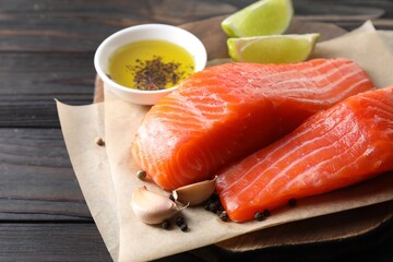 Pieces of fresh salmon, garlic, lime, oil and spices on wooden table, closeup