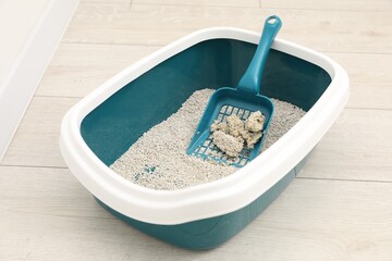 Cat litter tray with filler and scoop on floor indoors