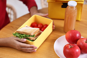 Wall Mural - Girl with lunch box of healthy food at wooden table in kitchen, closeup