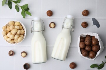 Bottles of macadamia milk and nuts on white tiled table, flat lay