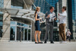 © qunica.com - Group of business professionals having an outdoor discussion in front of a contemporary office building, enjoying the sunny weather.