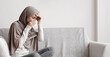 © Prostock-studio - Flu And Cold Concept. Sick Muslim Girl In Hijab Suffering From Temperature And Runny Nose, Feeling Unwell While Sitting On Sofa At Home, Copy Space