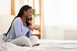 © Prostock-studio - Weekend. Happy Afro Girl Talking On Cellphone Sitting In Bed In Cozy Bedroom. Selective Focus, Empty Space