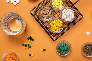 Wall Mural - Colored pills and tablets of dietary supplements in small glass bowls and a glass of water from above on an orange background. Groups of vitamins and minerals top view. Rustic style. Healthy lifestyle