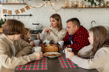 Family sitting at the table on a Christmas morning. Mother, father and their three children drinking tea and eating a cake for the Christmas breakfast.