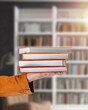 © BillionPhotos.com - Student hands hold a stack of books in library background.