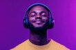 © PHB Stock - Music streaming platforms Image of a happy Black man in wireless headphones immersed in his favorite playlist eyes closed under neon lights against a purple backdrop panoramic vi
