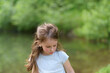 © PeterPike - Little cute preschool girl in a T-shirt plays on the background of a pond. Happy childhood concept outdoors