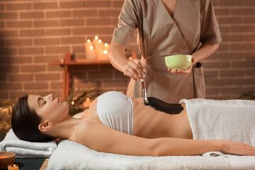 Wall Mural - Massage therapist applying mud on woman's belly in dark spa salon