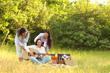 Canvas Print - Female friends playing guitar on picnic in park