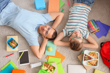 Poster - Little boy with his father in eyeglasses and school supplies lying on carpet, top view