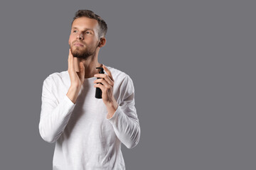 Sticker - Handsome young man applying cosmetics for beard on grey background