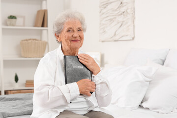 Wall Mural - Senior woman with Bible sitting on bed at home