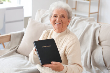 Poster - Senior woman with Bible sitting on sofa at home