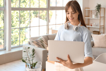 Canvas Print - Happy female student with headphones and laptop studying at home