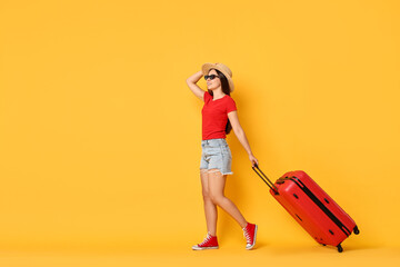 Wall Mural - Happy young woman in sunglasses with suitcase on orange background