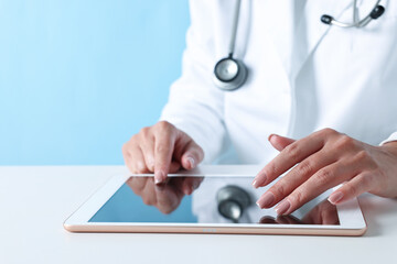 Poster - Doctor with tablet at table against light blue background, closeup view