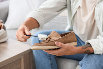 Wall Mural - Young man cleaning suede shoe with brush at home, closeup