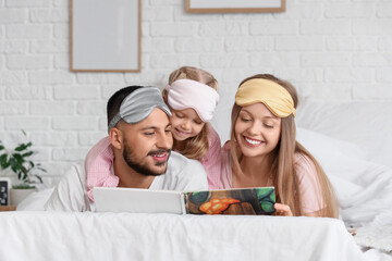 Wall Mural - Happy parents and their little daughter with sleeping masks reading book in bedroom