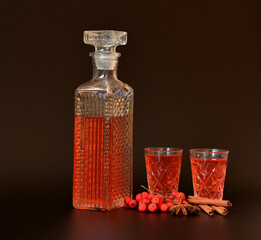 Rowan liqueur with cinnamon and anise on a black background, a crystal decanter and two glasses with strong alcohol next to spices and a bunch of ripe berries.