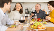 © JackF - Smiling young woman engaging in lively conversation with husband and elderly parents-in-law at family table with wine and fruits in cozy home kitchen