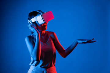 Wall Mural - Smart female standing surrounded by neon light wearing VR headset connecting metaverse, future cyberspace community technology. Elegant woman enjoy dancing wavering body and sing song. Hallucination.