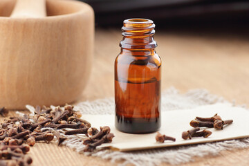 Cloves essential oil or extract in glass bottle with  spice buds on wooden table, closeup, natural medicine and healthy skin and body treatment concept