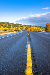 Highway road with yellow dividing strip abuts horizon with autumn forest on hills in Columbia River Gorge