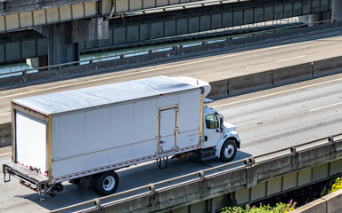 Local carrier day cab white middle duty rig semi truck with refrigerated box trailer with side door running for delivery on wide overpass highway road intersection