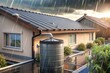© milanchikov - Casa equipada con un sistema de recolección de agua de lluvia en el tejado. El tanque conectado al techo captura el agua durante una tormenta, promoviendo el ahorro de agua y la sostenibilidad.