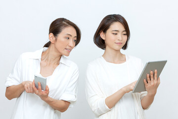 タブレットとスマートフォンを操作する母親と娘