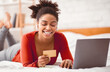 © Prostock-studio - Online Banking. Black Lady Customer Using Credit Card And Laptop Computer Lying In Bed At Home On Weekend. Selective Focus