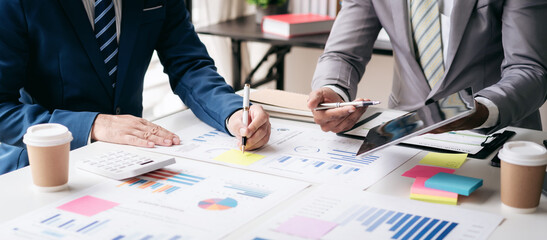 Fototapete - Two men in suits are sitting at a table with papers and a calculator