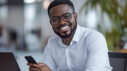 Successful businessman smiling while holding a smartphone, sitting at his office desk with a laptop Close-up photo with clean background