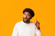 © Prostock-studio - Young african american shocked man having idea, pointing finger up, got problem solution, orange studio background, empty space