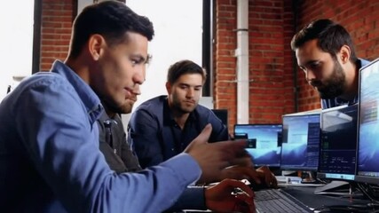 Four young men in a modern office, working on computers and having a discussion.