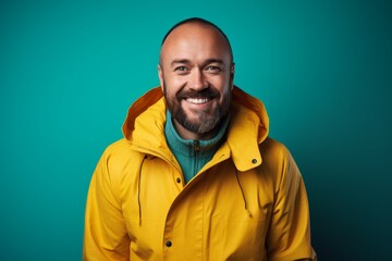 Wall Mural - Portrait of a smiling man in his 40s wearing a vibrant raincoat isolated on pastel teal background