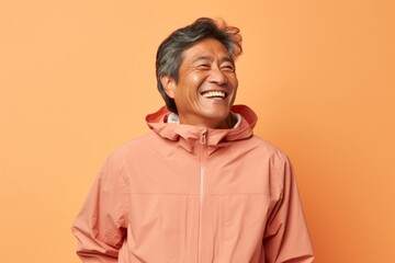 Canvas Print - Portrait of a joyful asian man in his 60s wearing a functional windbreaker over pastel brown background