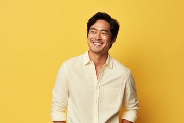 Wall Mural - Portrait of a joyful asian man in his 30s wearing a simple cotton shirt while standing against soft yellow background