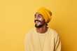 © Markus Schröder - Portrait of a blissful indian man in his 20s sporting a trendy beanie in front of soft yellow background