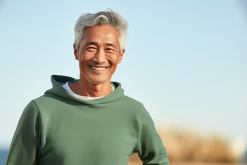 Poster - Portrait of a satisfied asian man in his 60s wearing a thermal fleece pullover while standing against soft green background