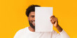 © Prostock-studio - Smiling african guy covering half of his face with blank paper over orange background