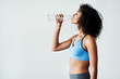 © StarDweller/peopleimages.com - Woman, training and drinking water in studio with fitness for hydration, break and thirsty of exercise with mockup. Athlete, person or liquid bottle for relax, wellness or refresh on white background