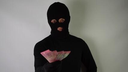 Wall Mural - 4k video footage of Dangerous young Adult black masked robber is holding a bunch of indonesian money and threatened people to demand money. 