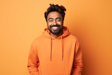 Poster - Portrait of a grinning indian man in his 20s sporting a comfortable hoodie over soft orange background